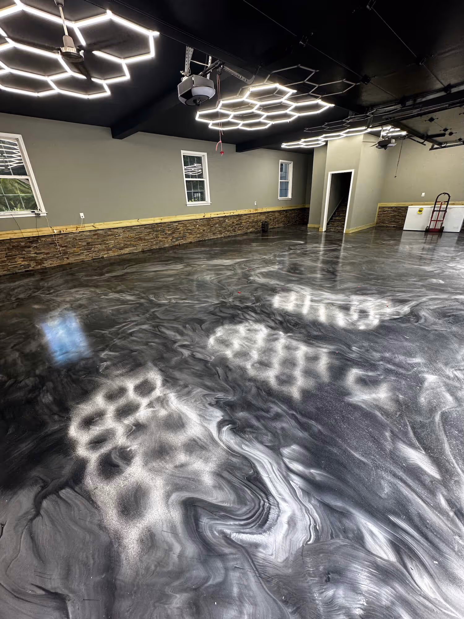 Spacious garage interior with shiny metallic epoxy floor in black and silver swirl pattern, illuminated by honeycomb-shaped ceiling lights in atlanta, ga