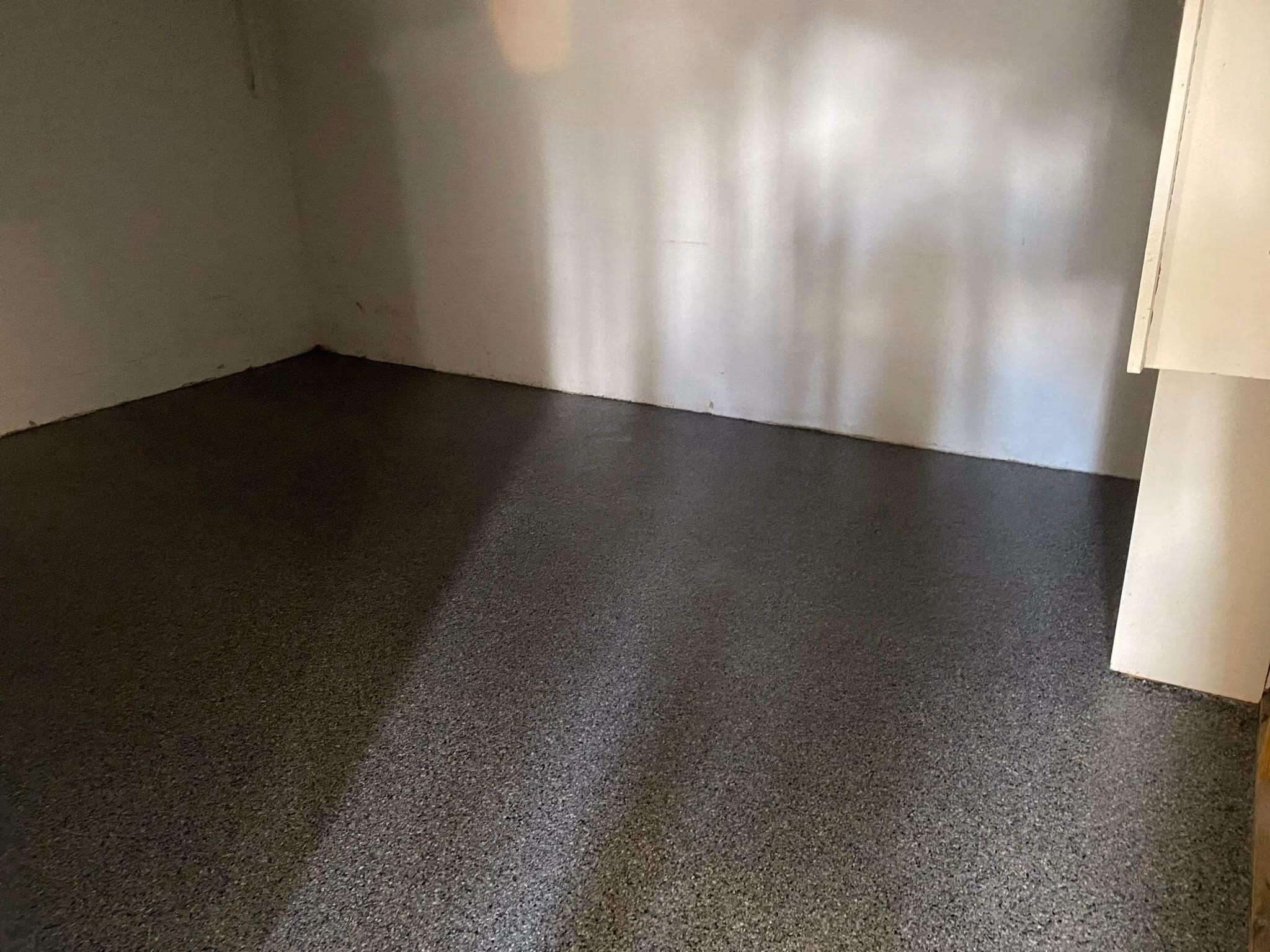 Empty room with a smooth, speckled quartz epoxy floor and plain white walls.