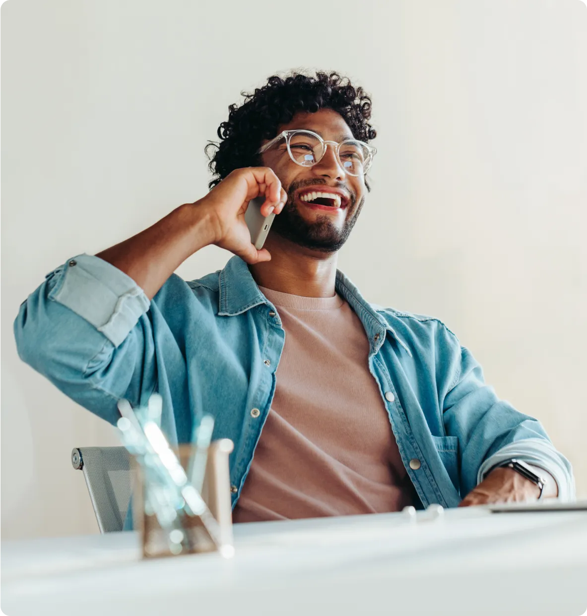 smiling man sitting at a desk talking on a cell phone