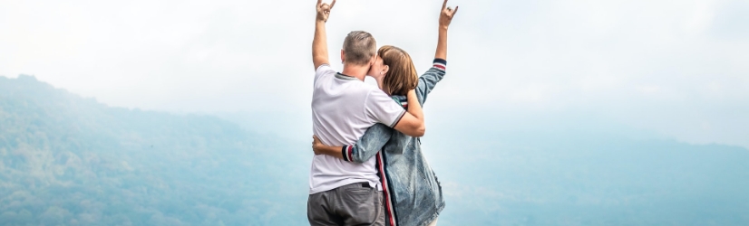 Ein Mann und eine Frau, die ihn küsst, beide halten Handzeichen und es ist ein Berg im Hintergrund
