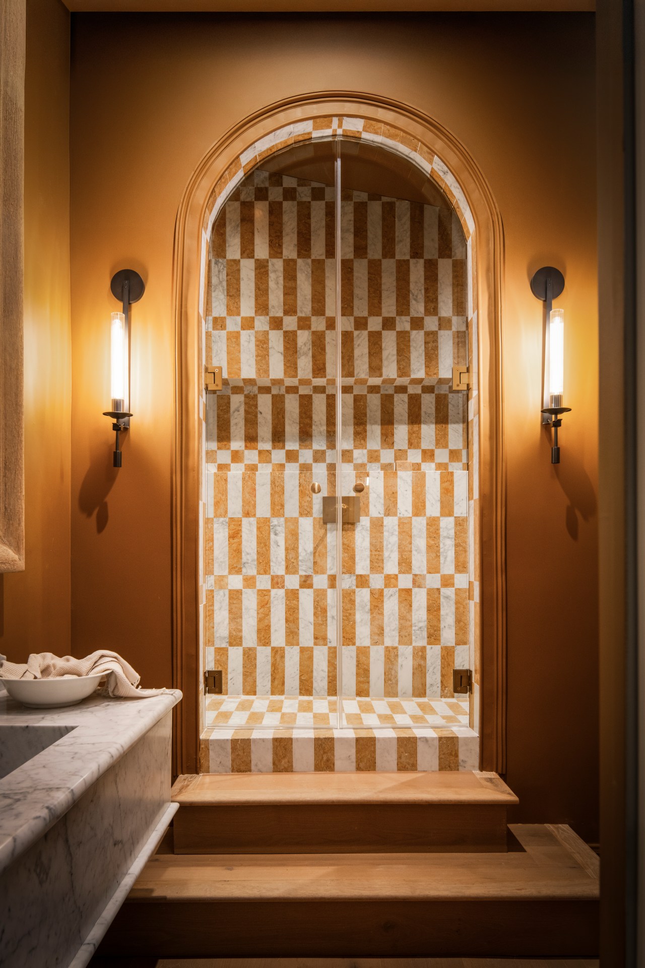 Photographed by Gavin Cater. “The space is a study in geometry, with mustard-yellow and Carrara marble tiles laid in alternating stripes that shift direction across the floors and walls. The effect is immersive, and stepping inside feels like walking into a piece of art,” says Leigh and Hahn. Along with the elevated shower, it’s the rooms’ balance of playfulness and refinement that has made it one of the most beloved design moments of the home.