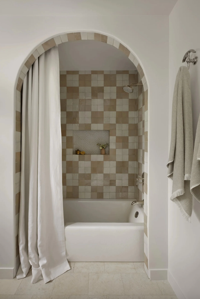 Arched shower nook with checkered tiles, white curtain, and hanging towels.