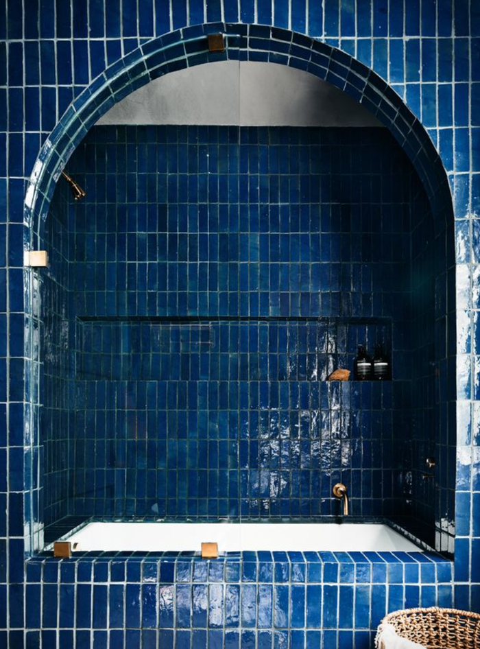 Arched blue-tiled bathroom with a bathtub and built-in shelf.