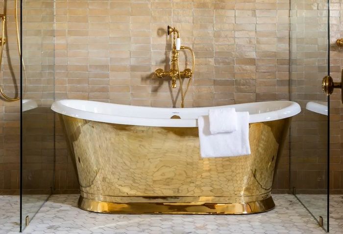 Luxurious gold bathtub with a white towel, set against tan wall tiles.