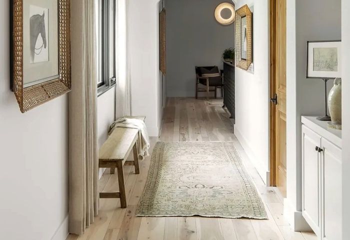Bright hallway with a wooden bench, framed art, and a patterned rug on light wood floors.