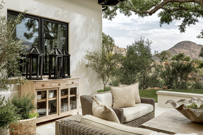 Outdoor patio with wicker sofas, wooden cabinet, lanterns, and scenic mountain view.