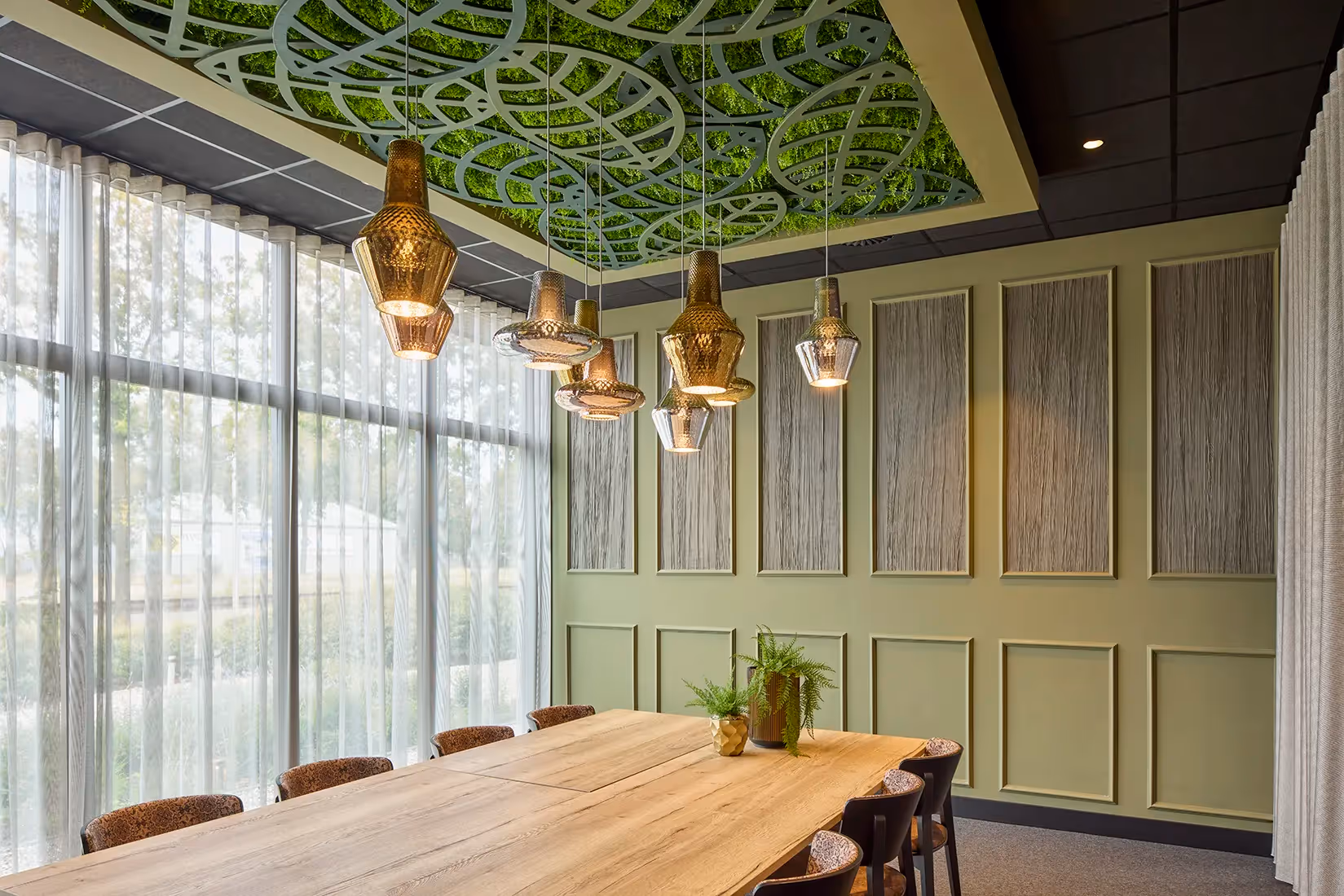 Diner en vergaderuimte met gegroepeerde hangarmaturen boven een grote tafel.