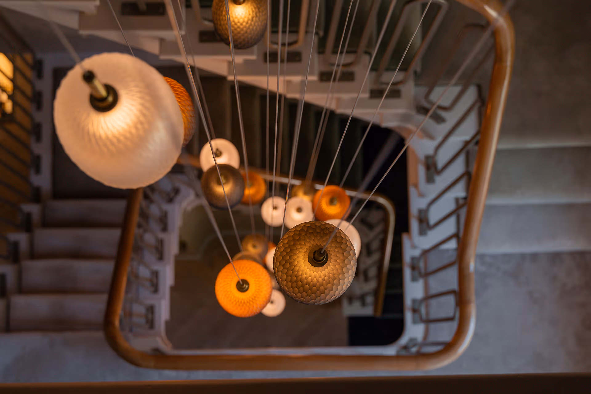 Bovenaanzicht van volle hoogte van een trappenhuis, met gegroepeerde hanglampen met handgeslepen glazen oppervlak.