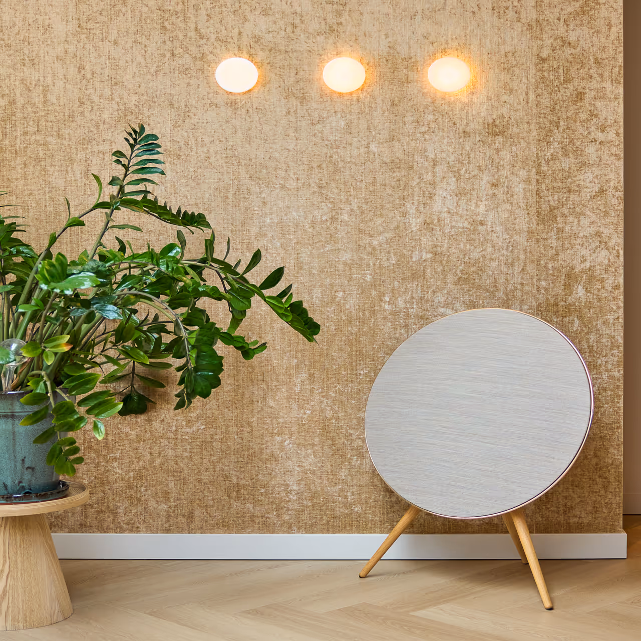 Drie cirkelvormige wandlampen verspreiden zacht diffuus licht boven goudgetinte wand met plant.