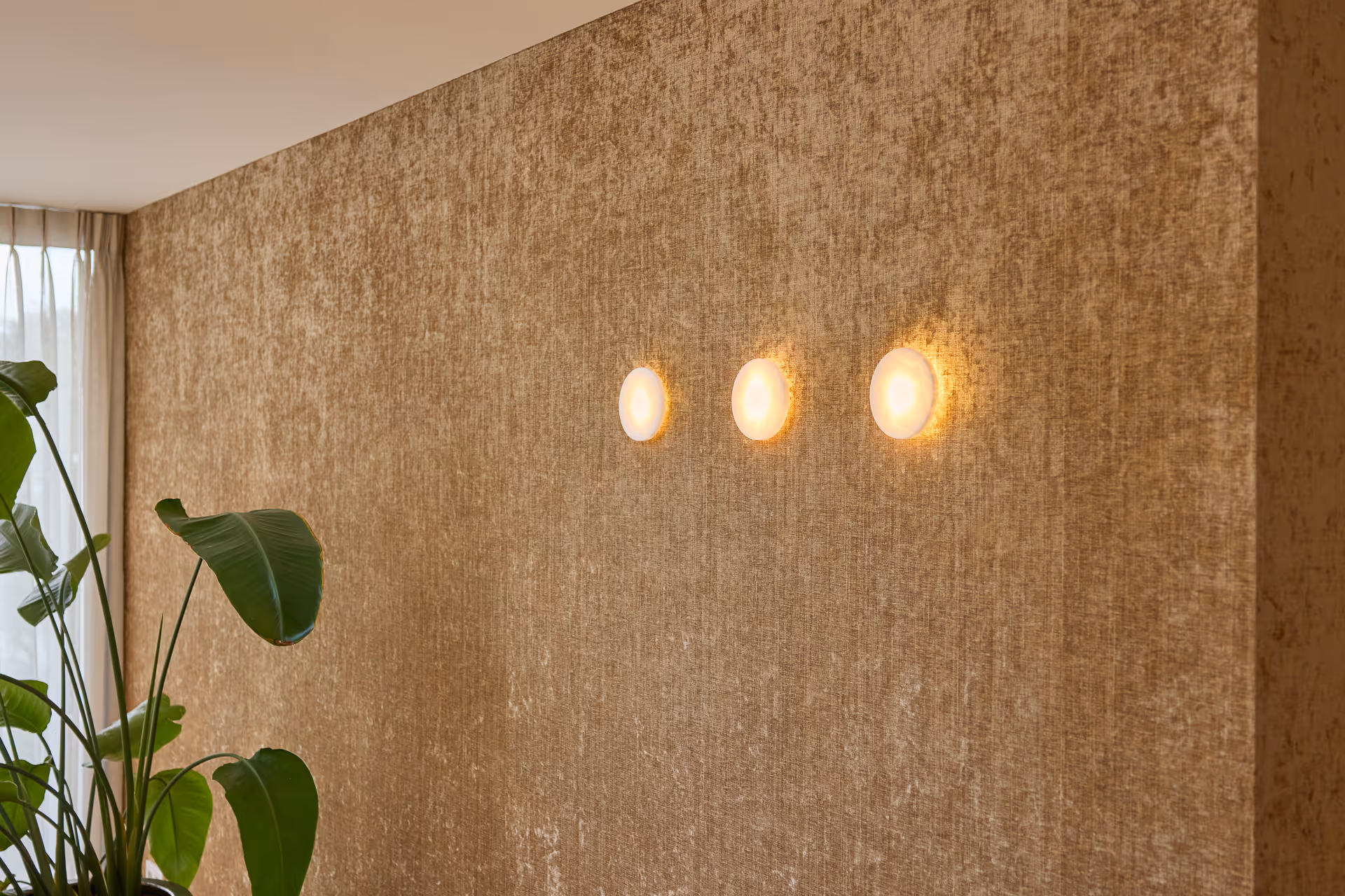 Drie ronde wandarmaturen op goudkleurige wand creëren diffuus licht en ritmisch patroon.