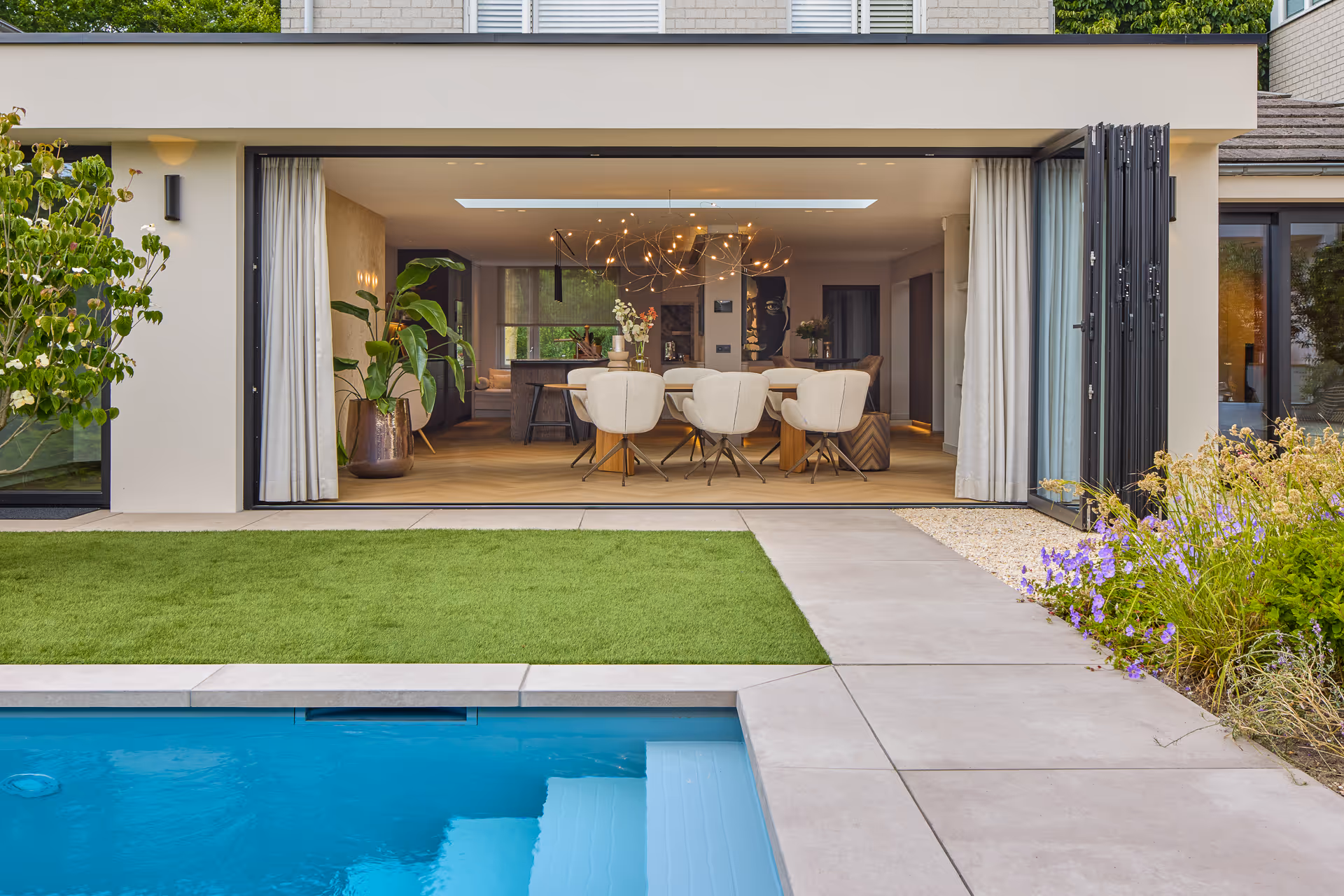 Zichtlijn vanuit tuin naar open eethoek met sculpturale hanglamp.