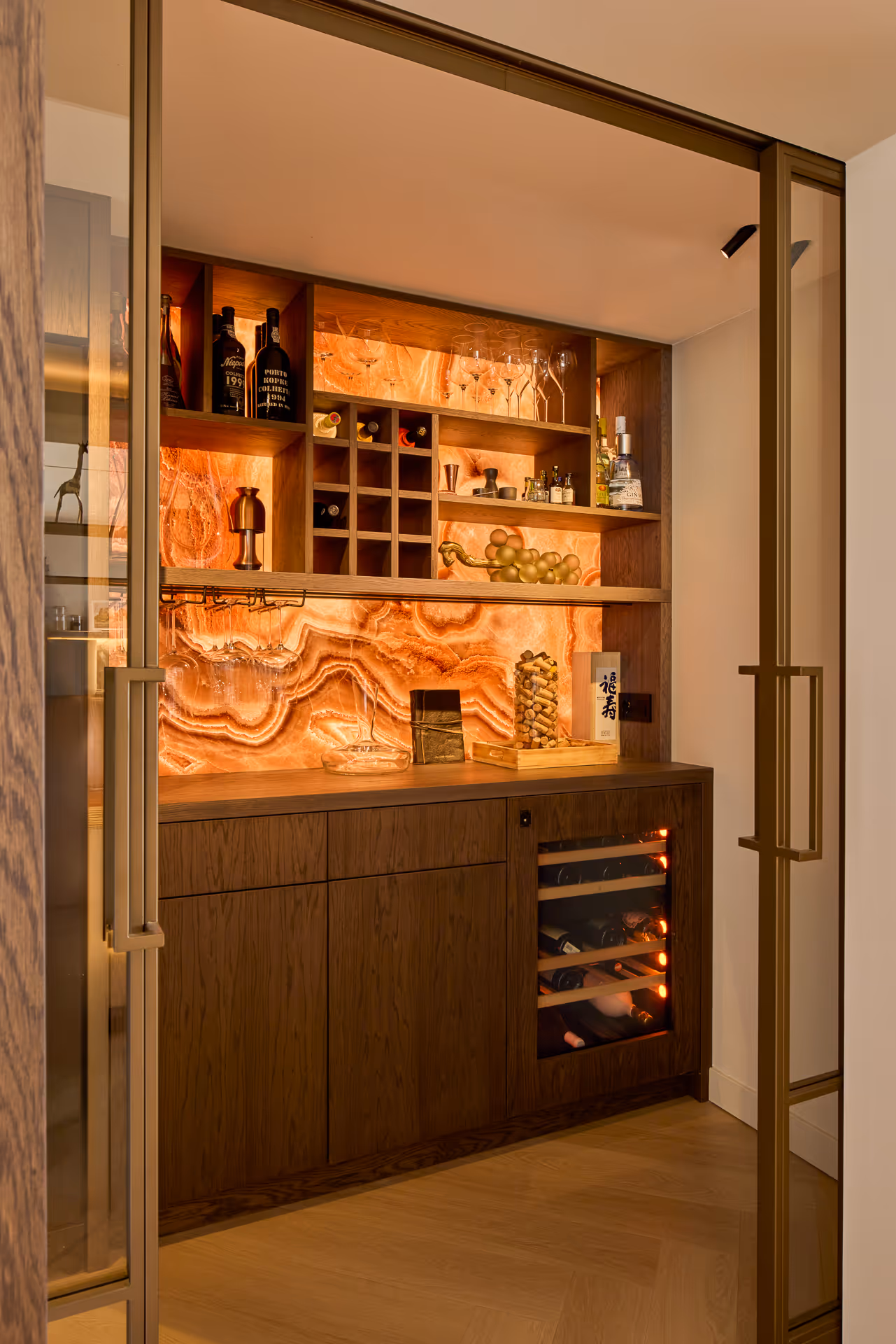Wijnkamer met houten kasten en geïntegreerde wijnrekken, voorzien van met sfeervol licht door richtspots die achterwand warm uitlichten.