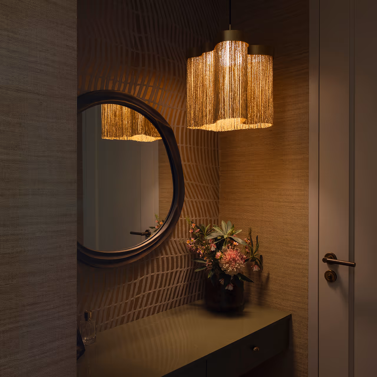 Hal met sierlijke hanglamp van gouden franjes boven console, spiegel en bloemstuk in warme sfeerverlichting.