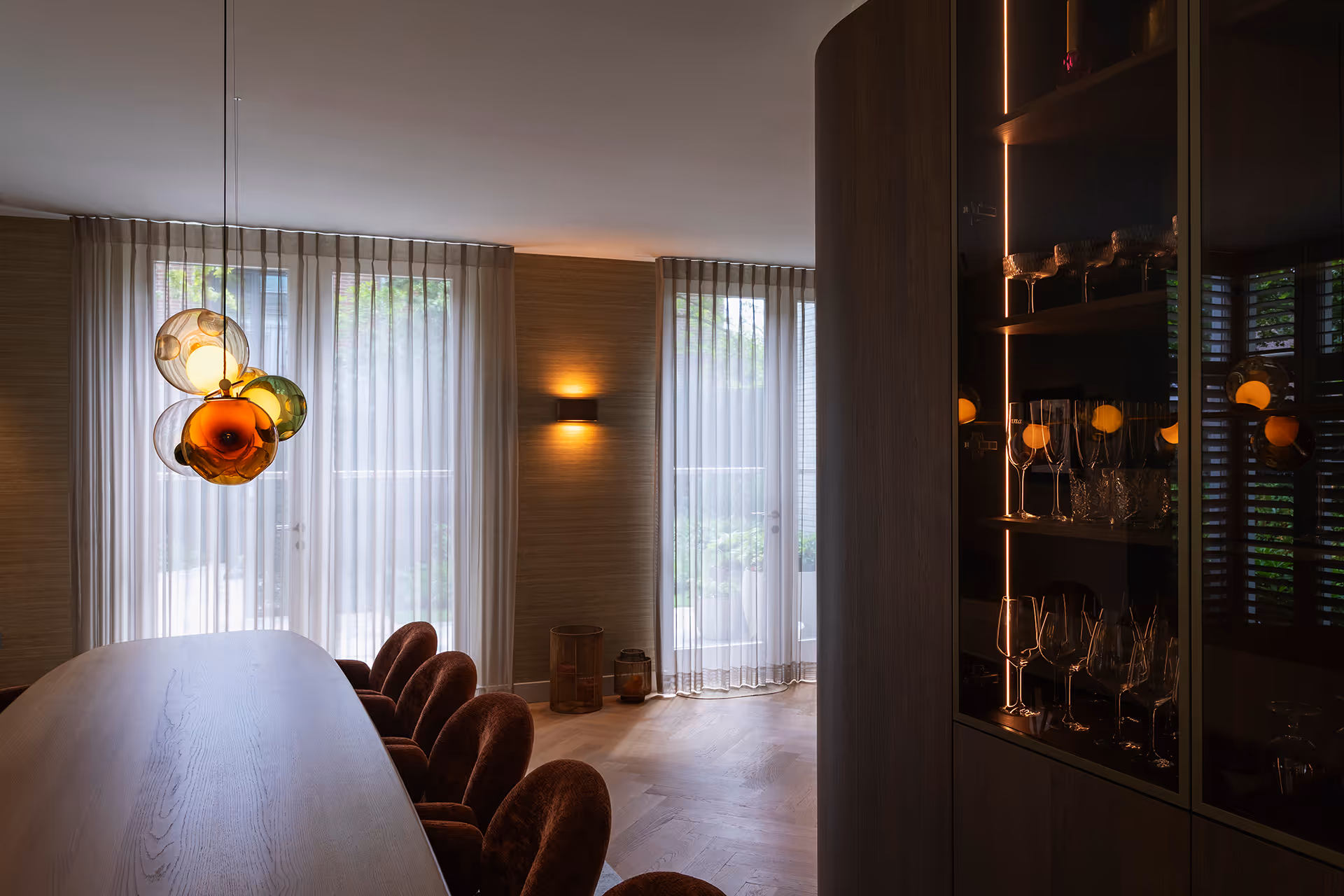 Detail van glasklusterarmatuur met amber- en groentinten, waar licht door het glas een speels kleurverloop creëert.