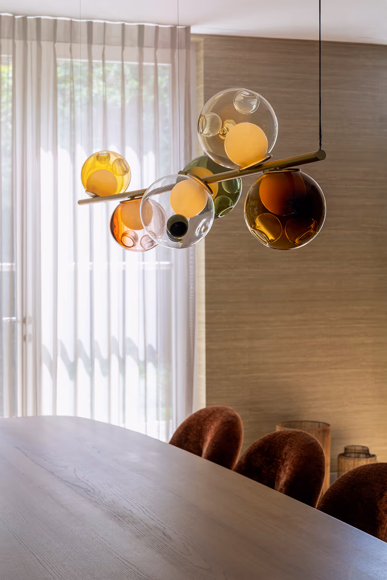 Eetkamer met ovale houten tafel, fluwelen stoelen en hanglamp met glazen klusters die warm licht verspreiden.