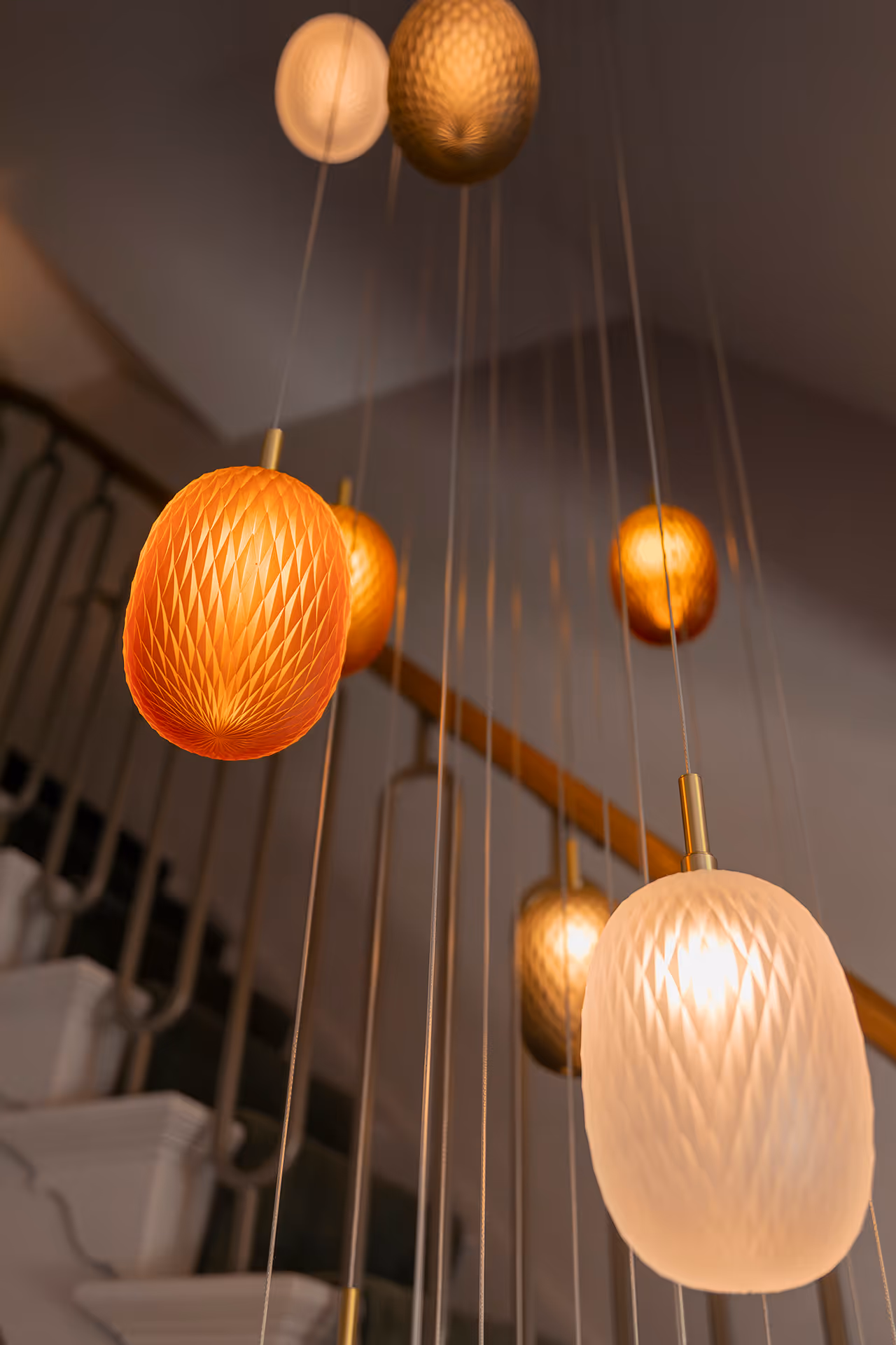 Close up van glazen hanglampen in trappenhuis in warme tinten met verspreiding van zacht licht.