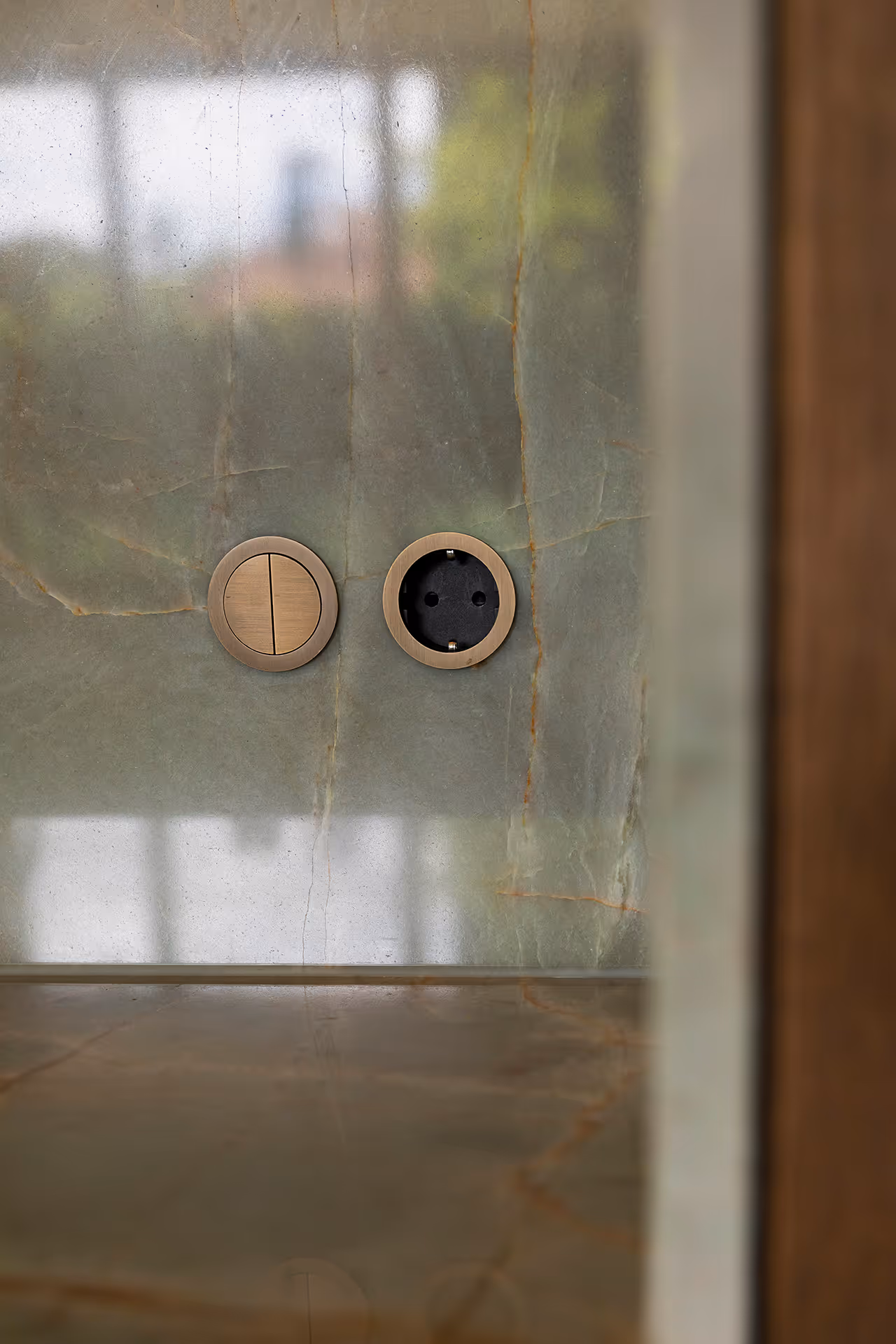 Detail van groenmarmeren keukenwand met verzonken en strak afgewerkt messing schakelaar en wandcontactdoos.