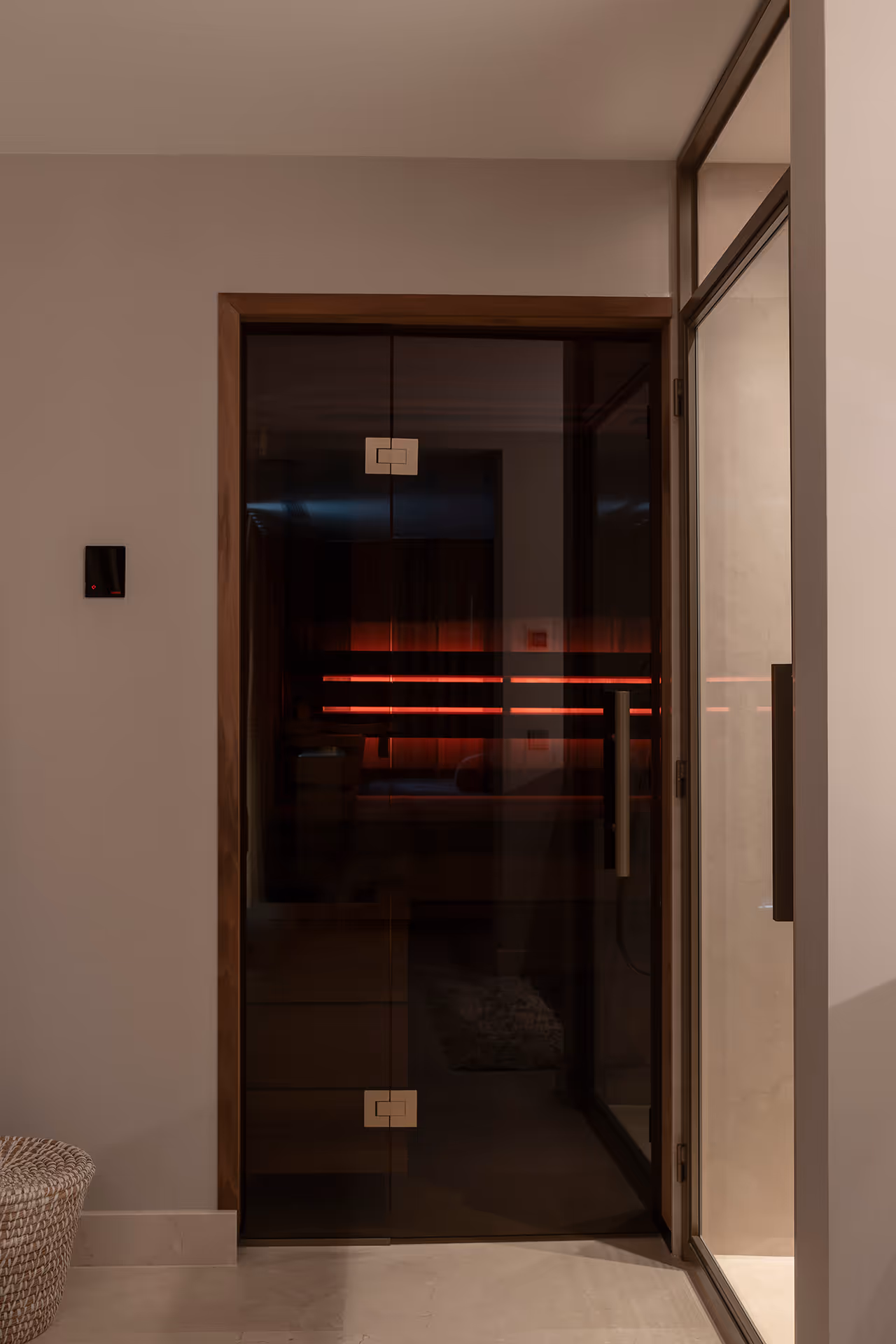 Glazen saunadeur met reflectie van rode ledverlichting in een warme, minimalistische badkamer.