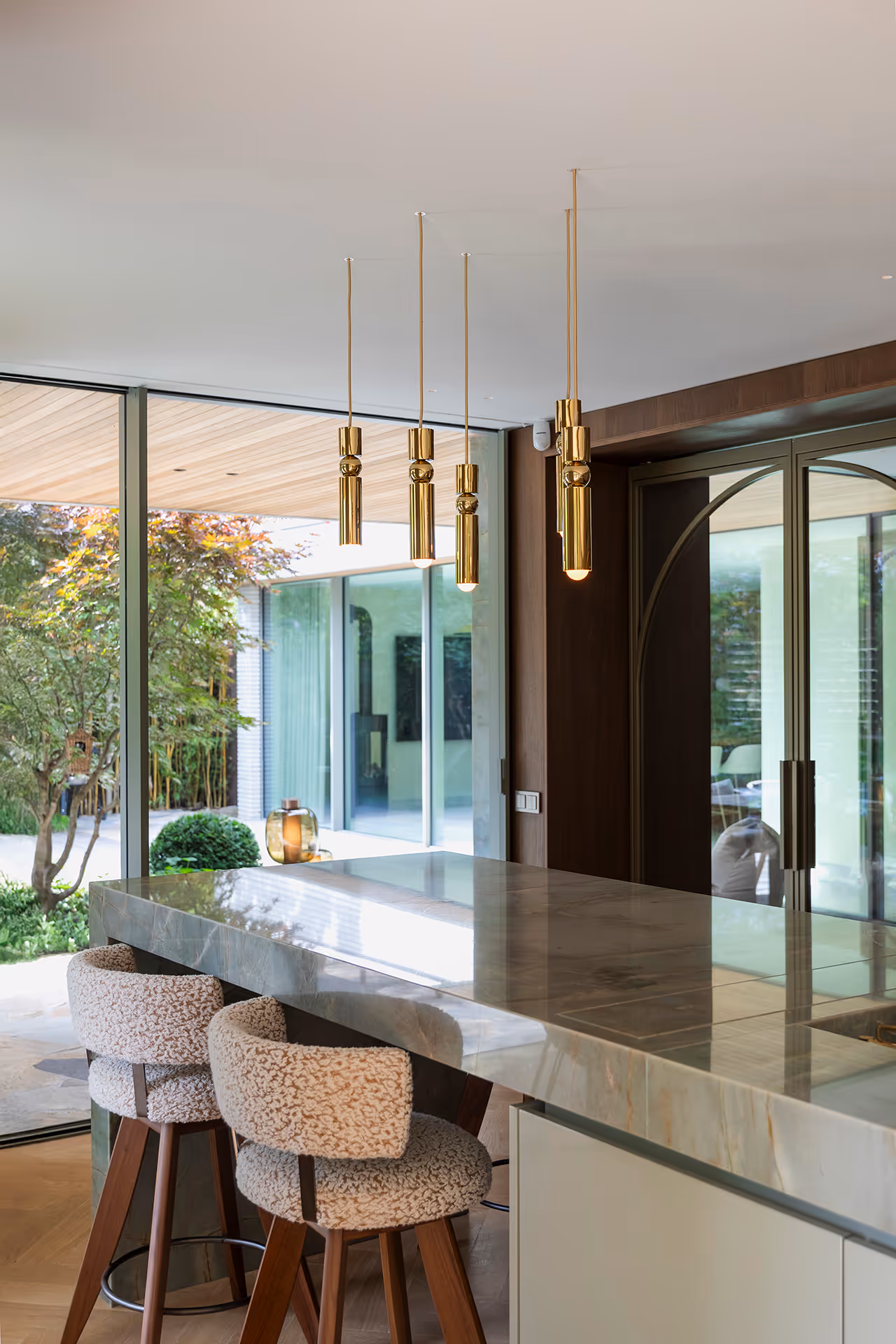 Keuken met groot marmeren blad met goudgekleurde hanglampen die het warme interieur versterken.