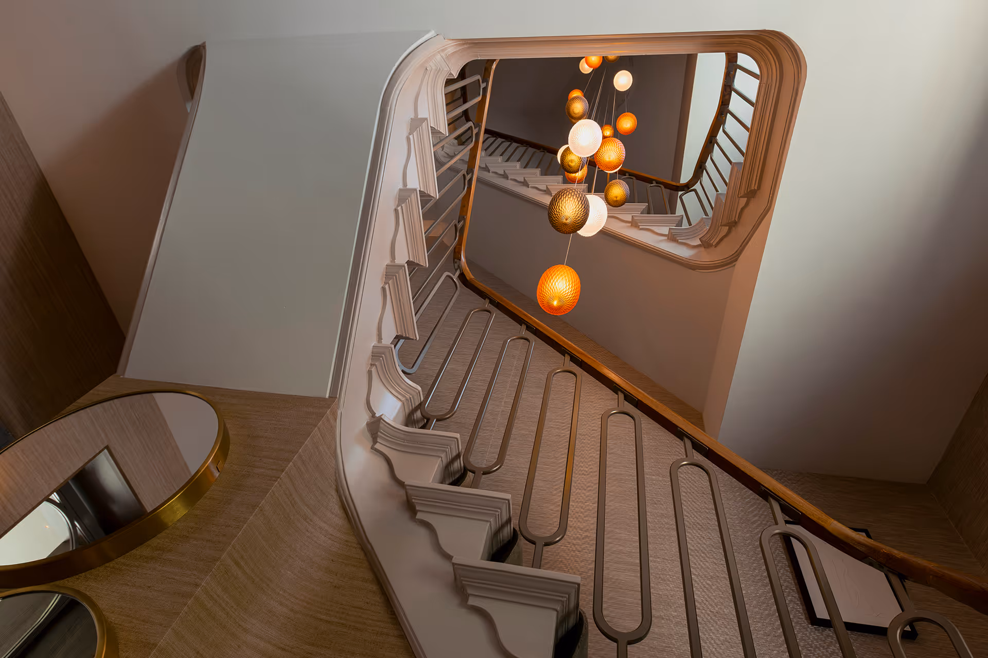 Onderaanzicht trappenhuis toont sculptuur van geclusterde hanglampen in warme kleurtonen.
