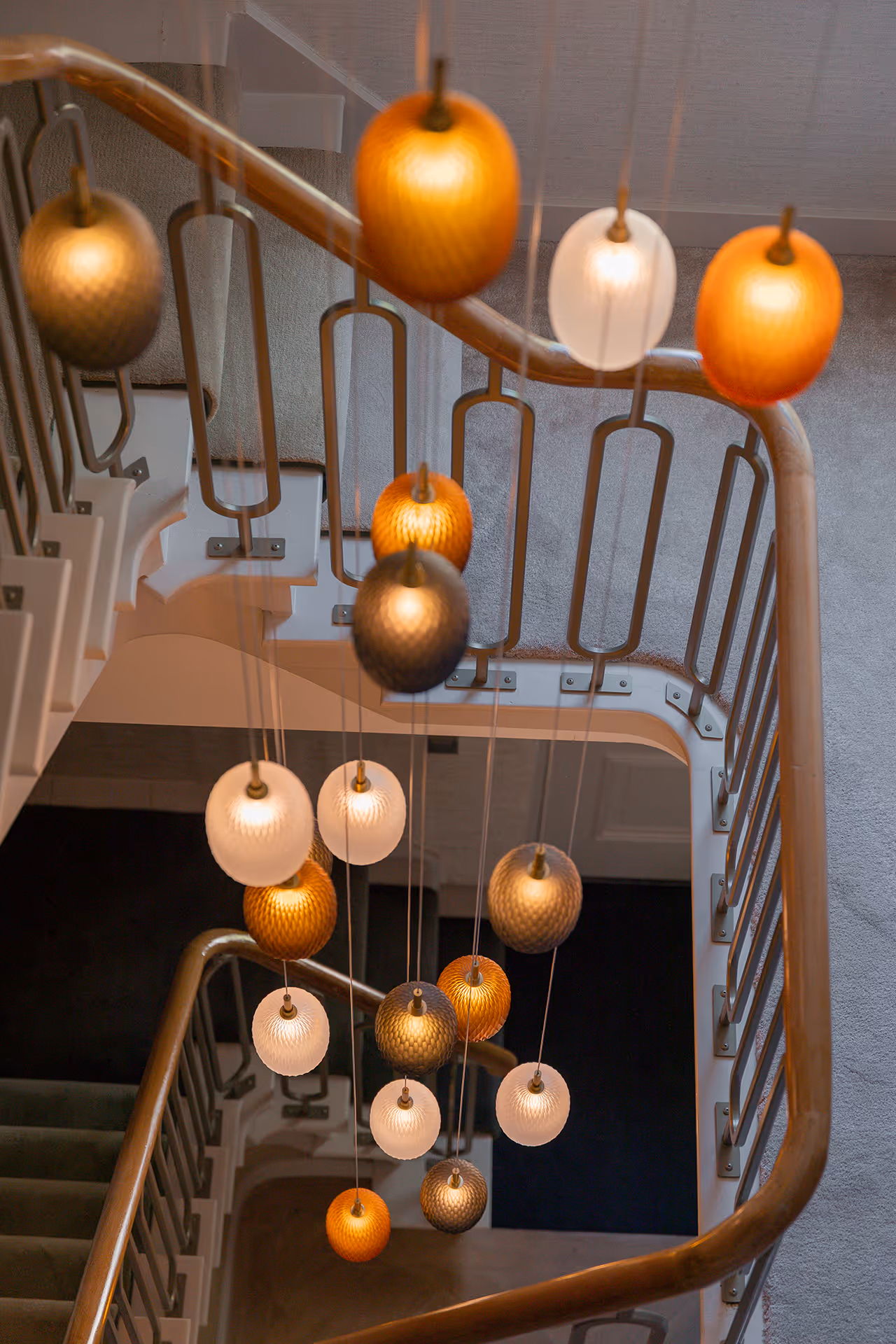 Cluster van glaspendels met amber en wit glas die warme lichtreflecties creëren langs de trapleuning.