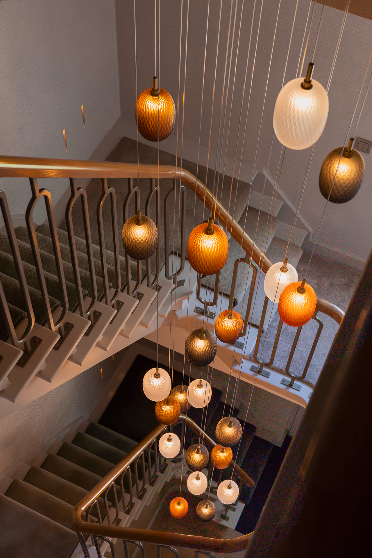 Lichtinstallatie van hanglampen gezien vanuit trapleuning, met contrasterend spel tussen licht en schaduw.