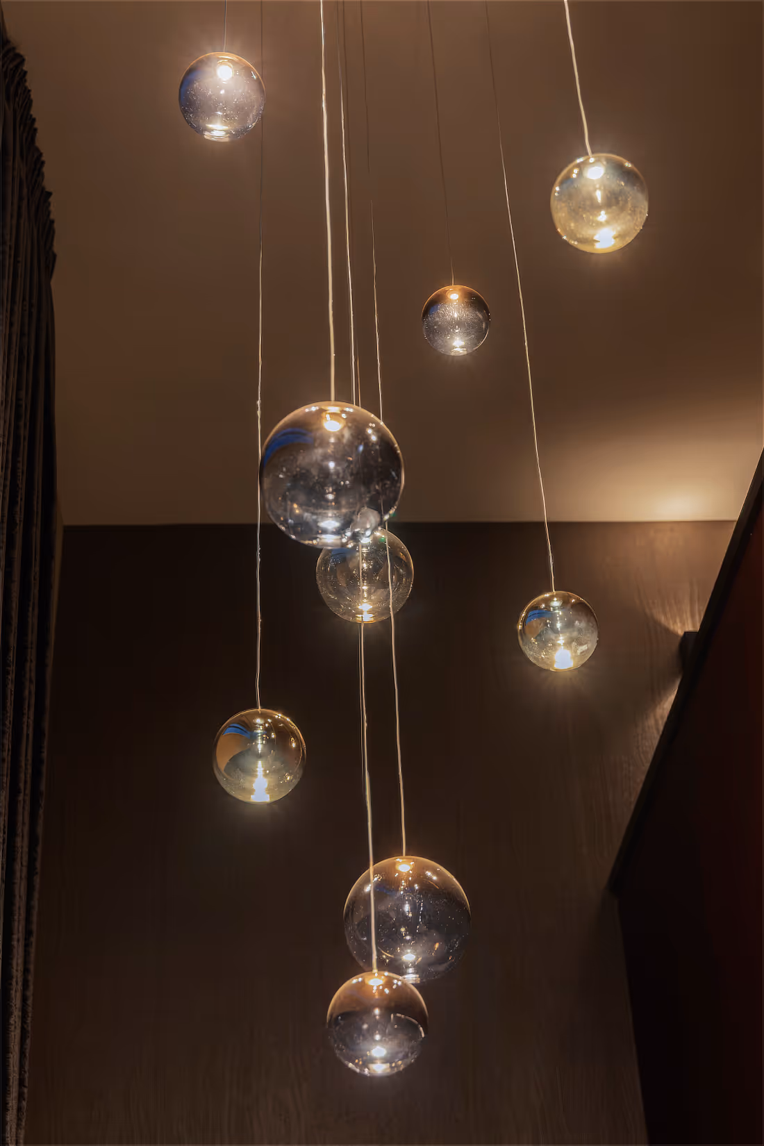 Cluster van glazen bolpendels creëert speels lichtbeeld in de vide.