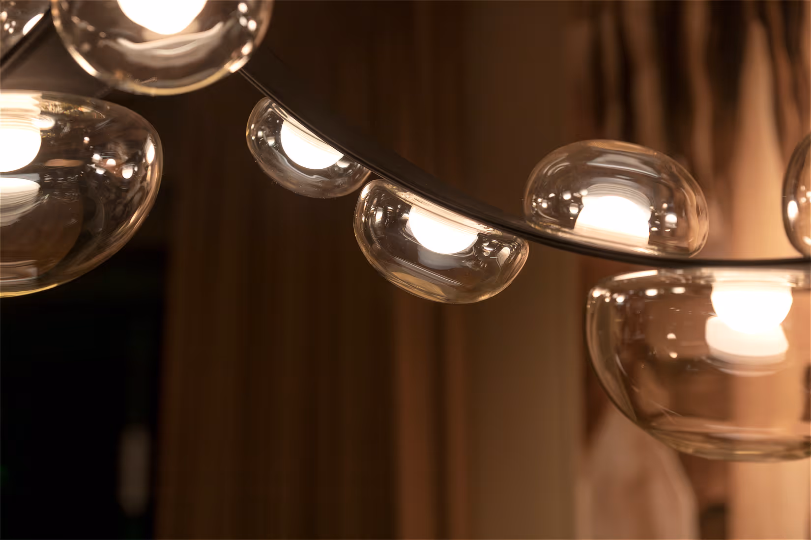 Close-up van lederen hangarmatuur met glazen druppelgevormdelichtmodules in warme tint.