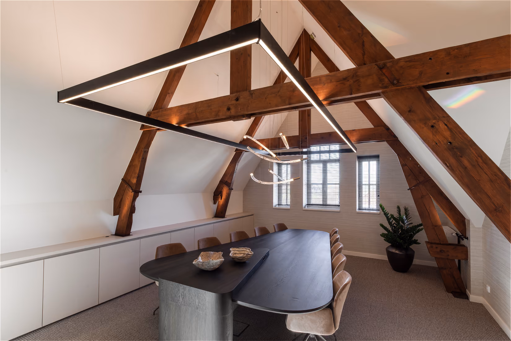 Breed zicht op de vergaderruimte met een lineair lichtframe en de sculpturale hanglamp van gebogen buizen.