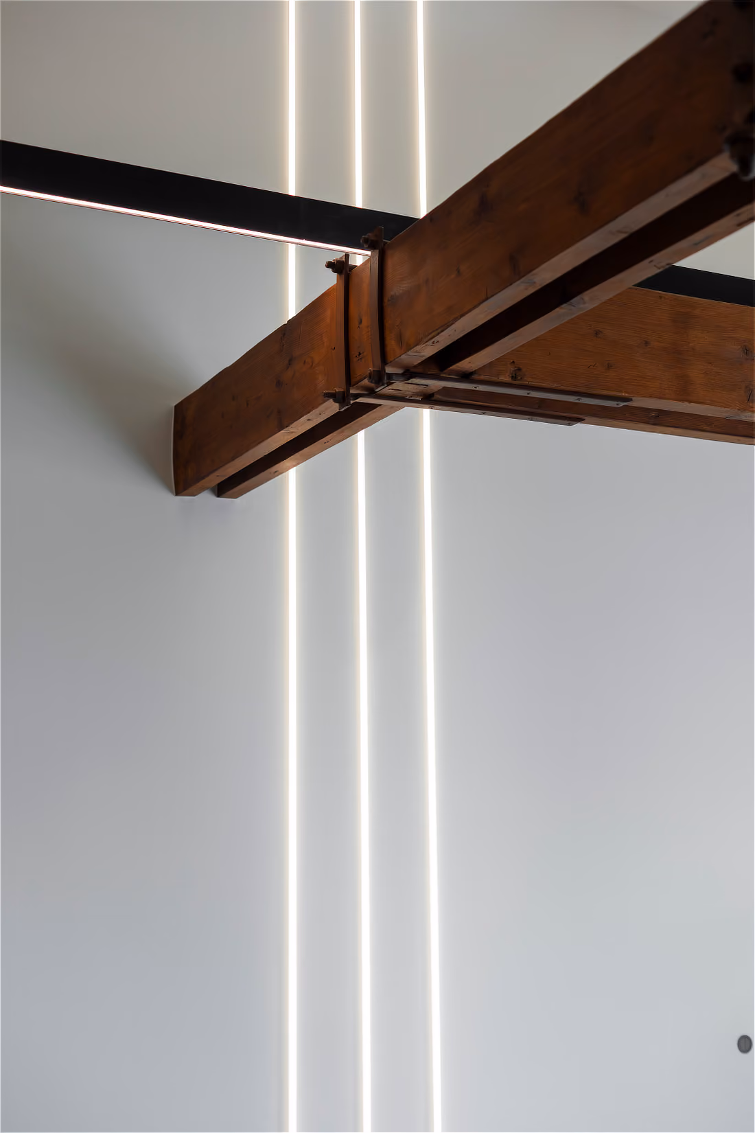 Drie verticale lichtlijnen onder een verbindingspunt van twee massieve houten balken.