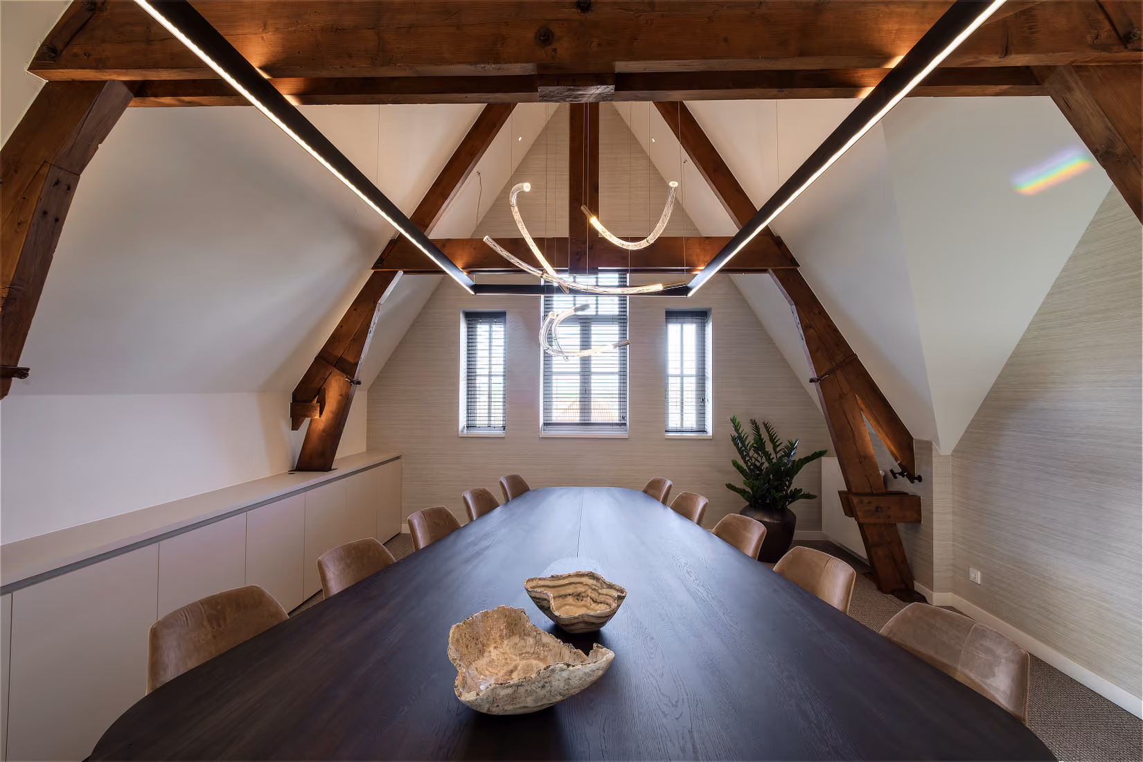 Lange vergadertafel, verlicht door een sculpturale hanglamp met gebogen buizen.