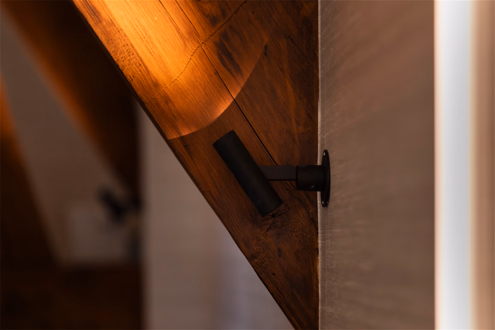 Detail van een richtspot die een houten dakcontructiebalk verlicht met warm strijklicht.