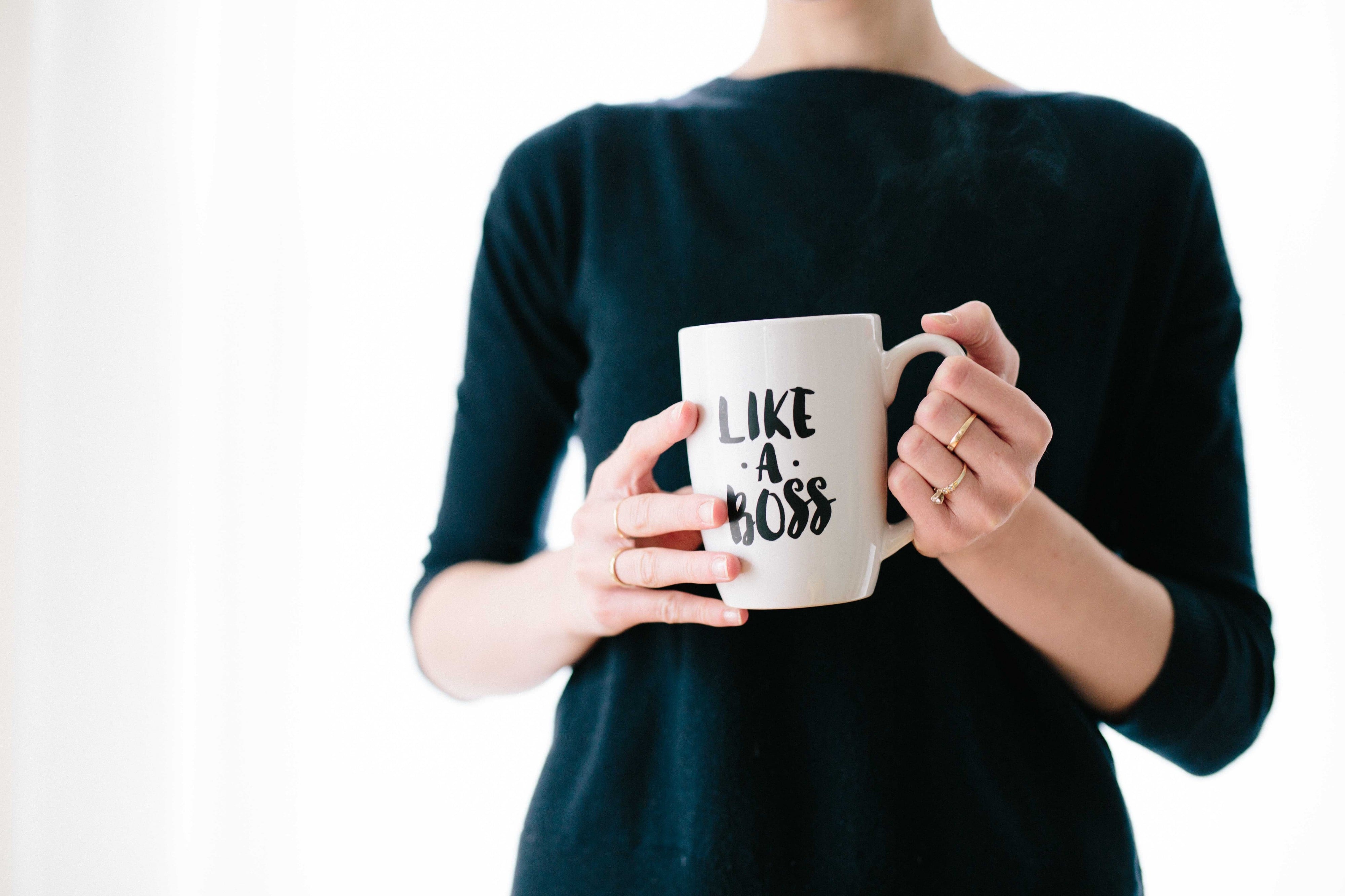 A woman holding a coffee mug which has a sign "Like a Boss", photographed by Brooke Lark.