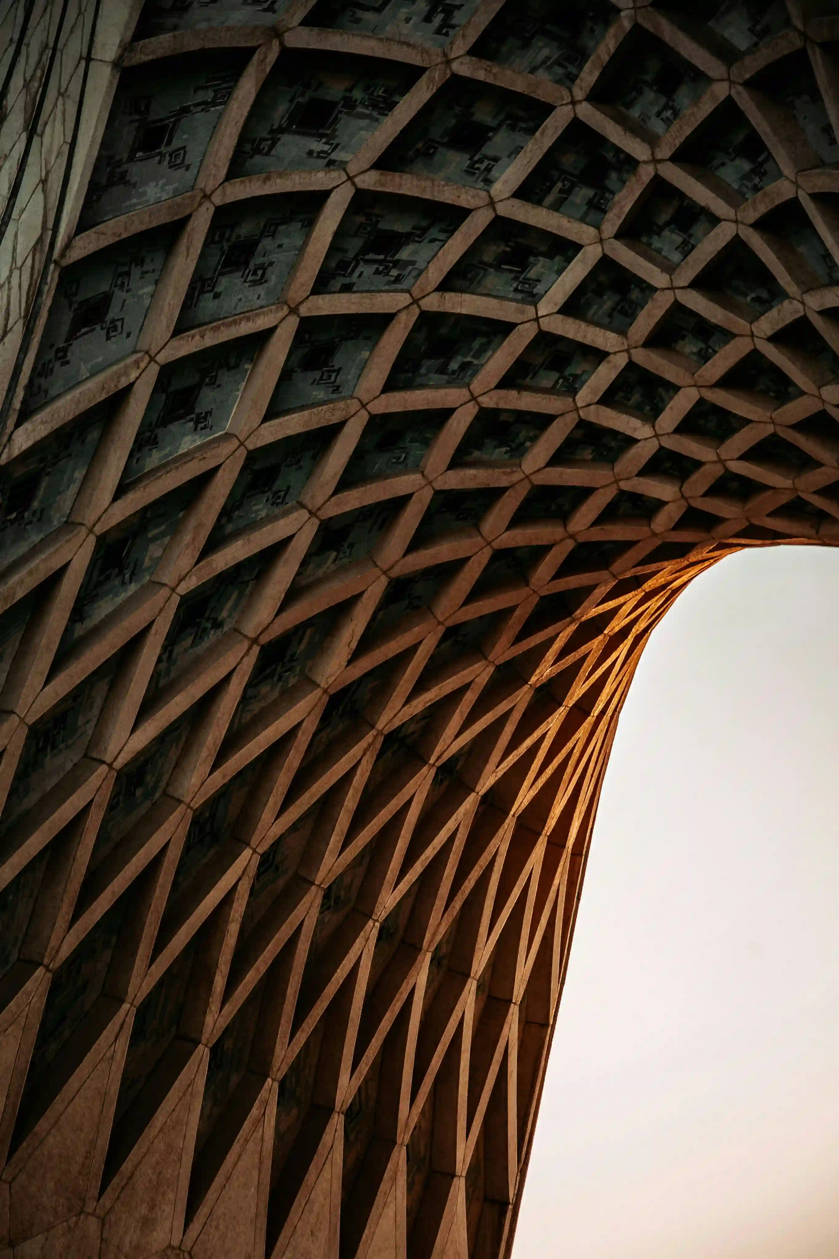 Curved lattice patterned architectural structure with sunlight highlighting edges against clear sky.
