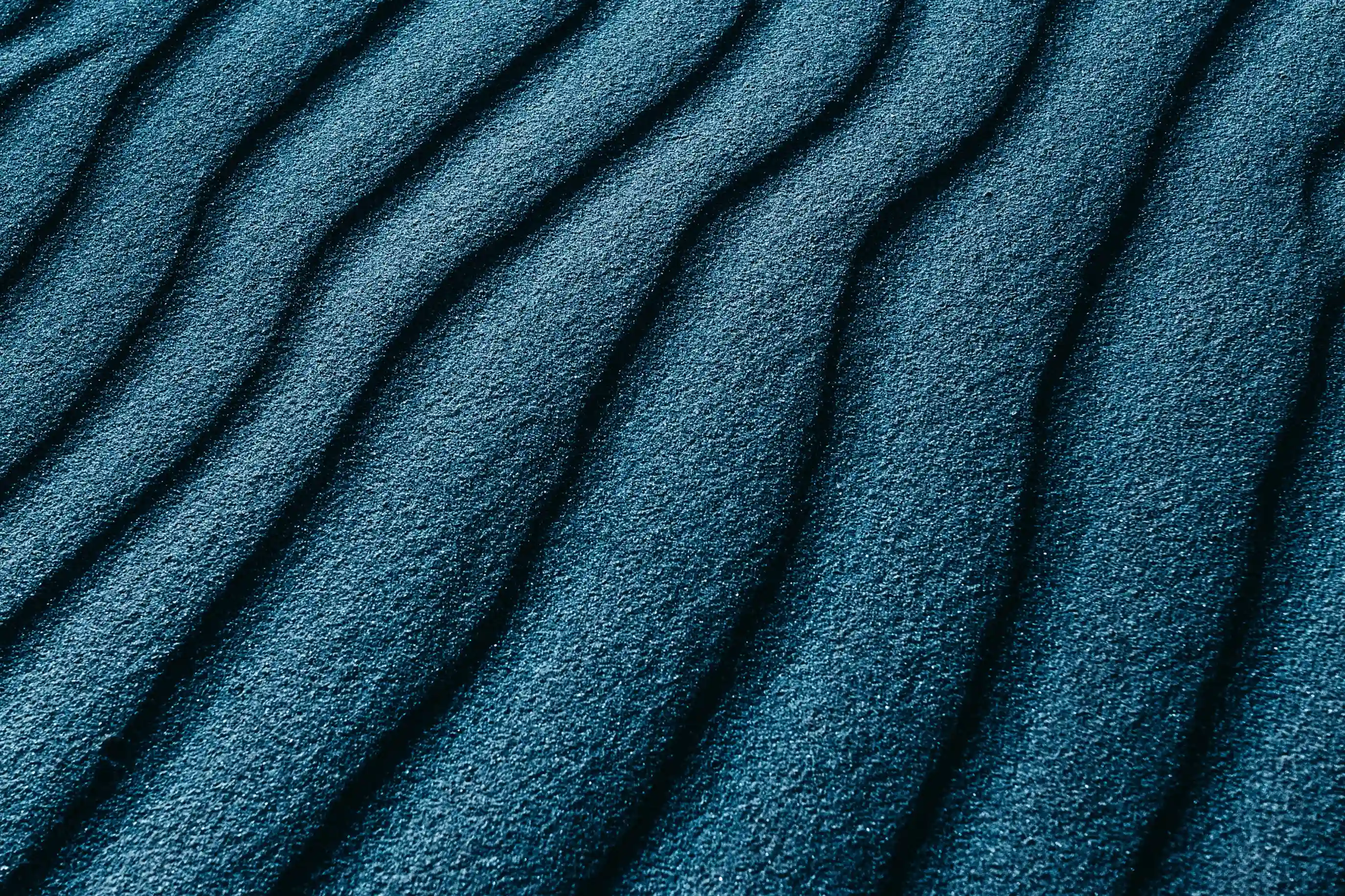 Close-up of blue sand ripples forming parallel curved lines.