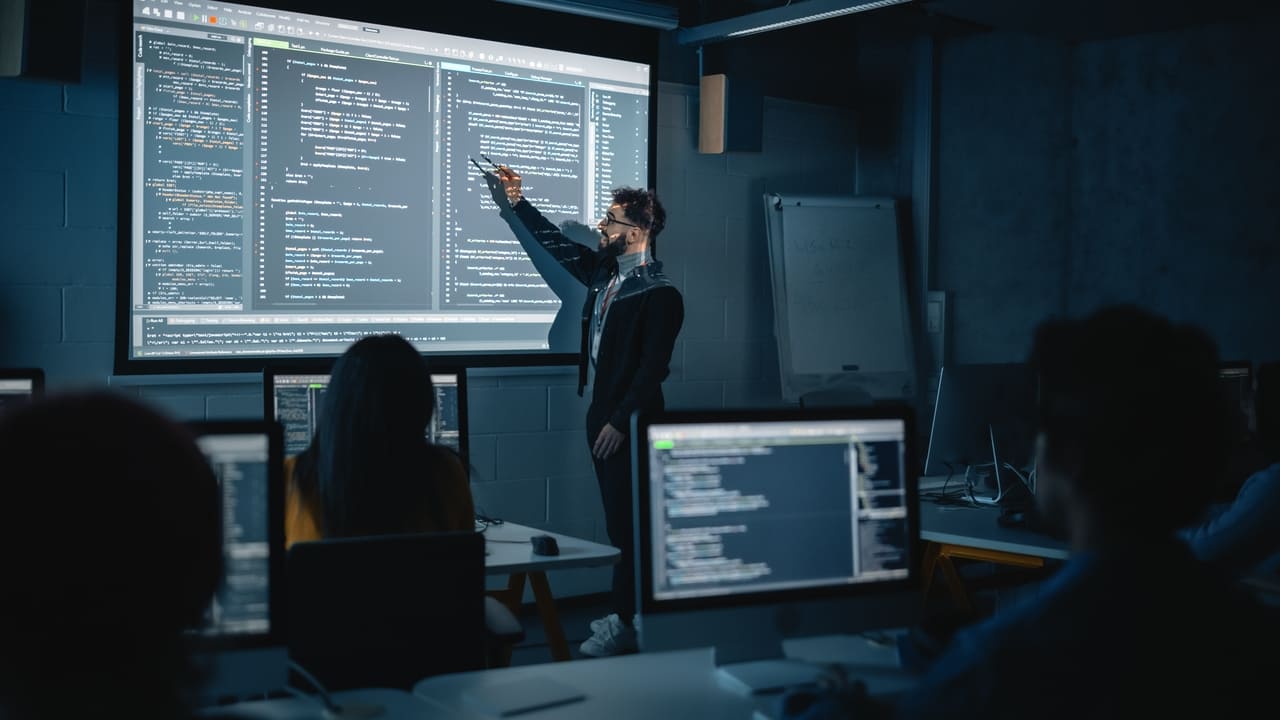 Instructor presenting AI-powered educational software in a classroom with code and system outputs displayed on a large screen.