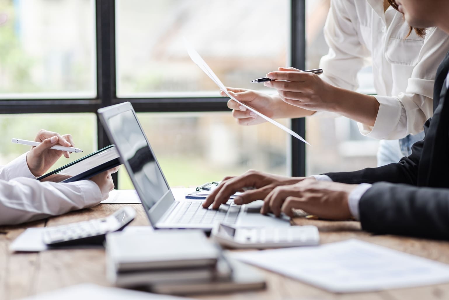 Team members at a meeting table reviewing printed documents and notes beside an open laptop in a bright office setting.