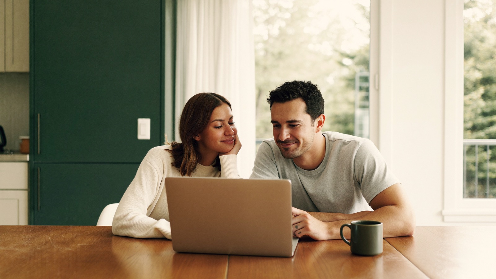 A couple in their thirties looking at a laptop together at a clean kitchen table in a Vancouver home