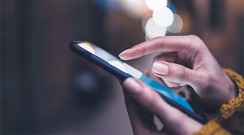 Close-up of a person using a smartphone with a blurred urban background at night.