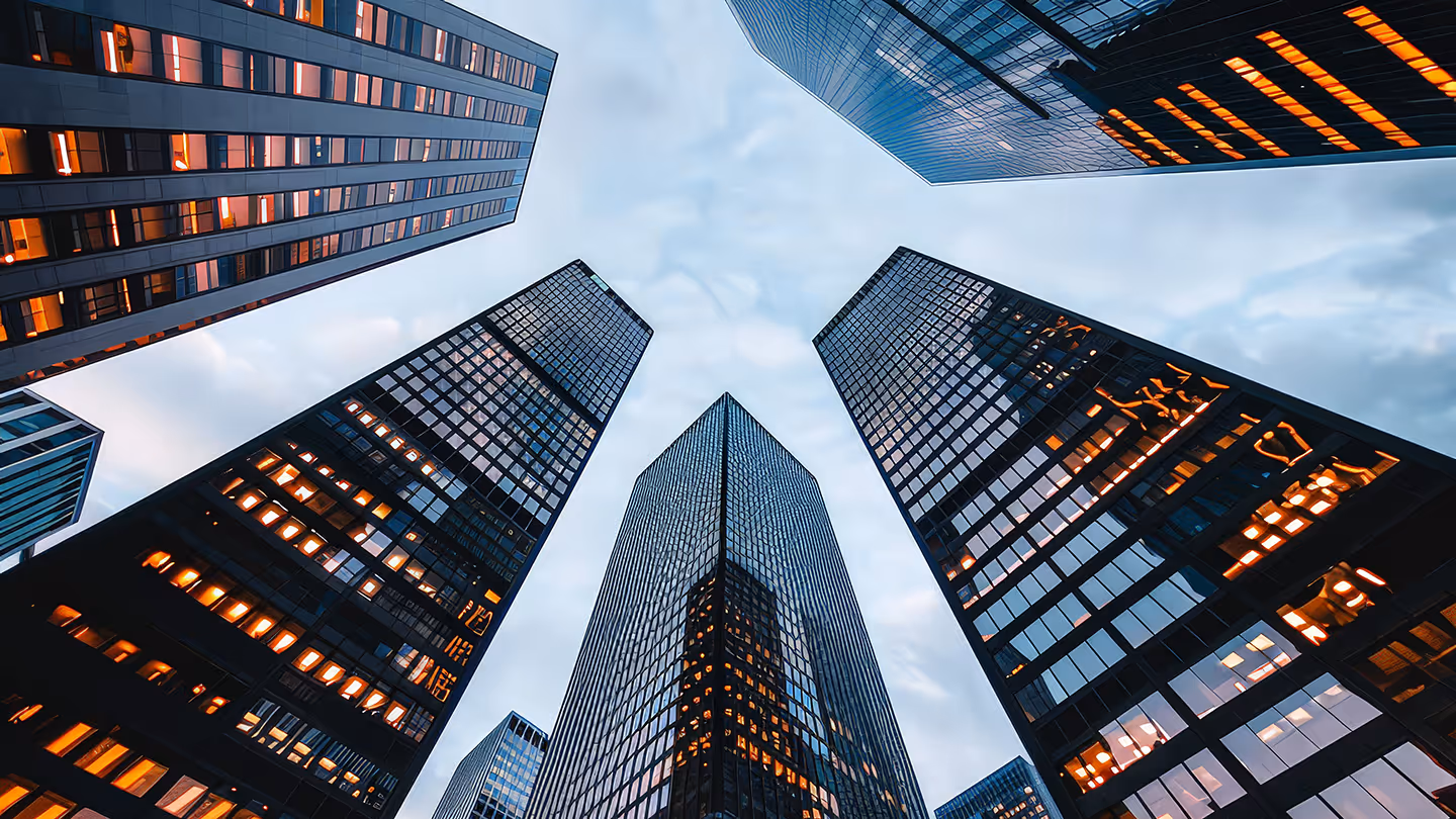 Low-angle view of modern skyscrapers with lit windows under a cloudy sky in a cityscape.