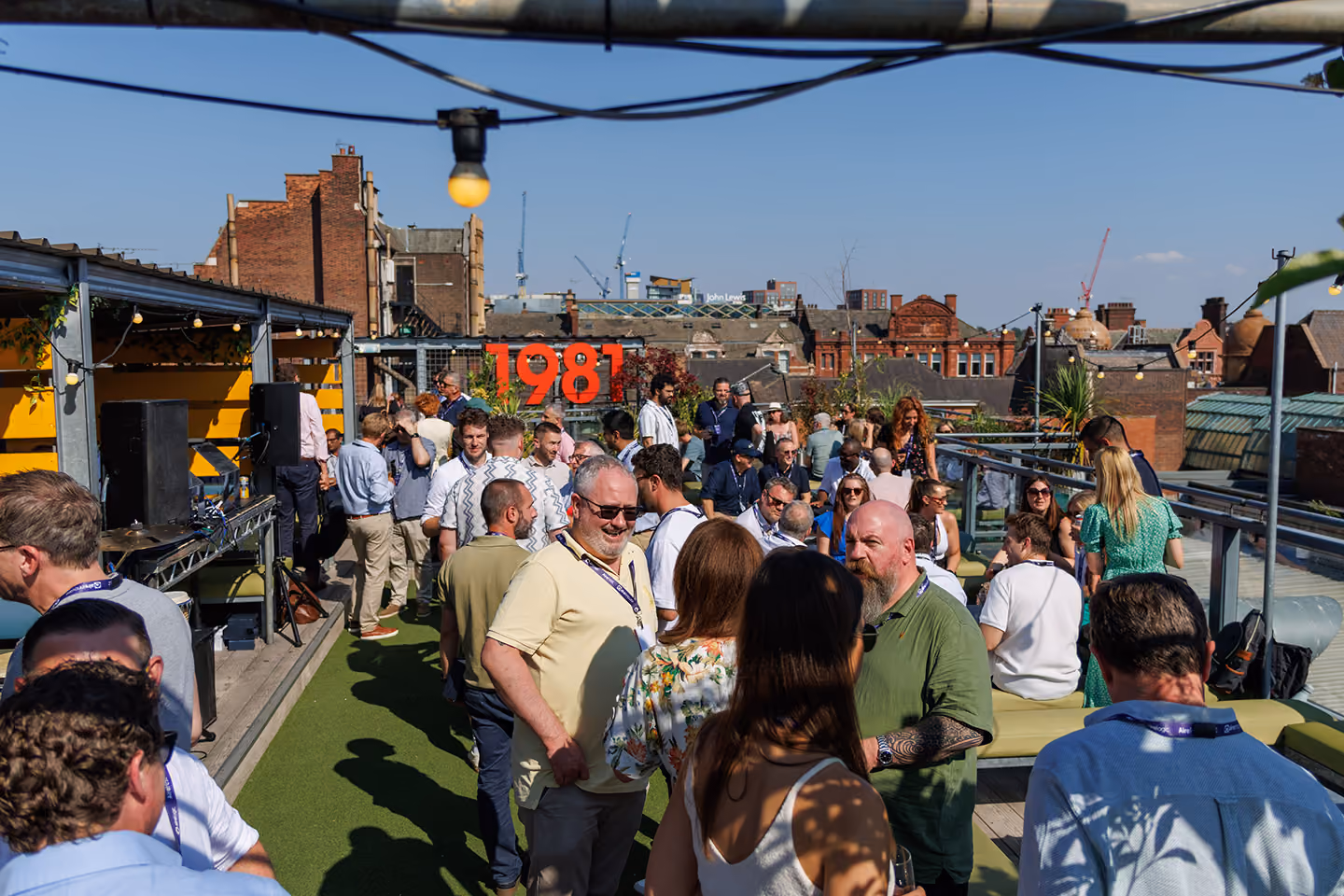 People socializing on a rooftop terrace with city buildings and blue sky in the background.