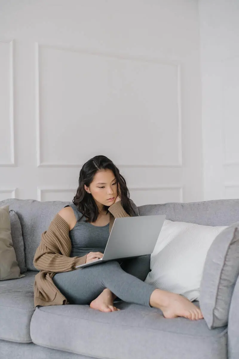 A woman sitting on a sofa looking at her laptop screen.