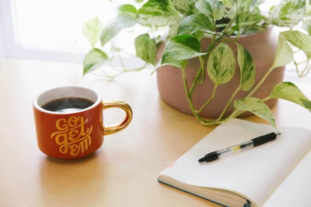 "Go get 'em" design on a cup filled with fresh coffee next to a notebook and pen. 
