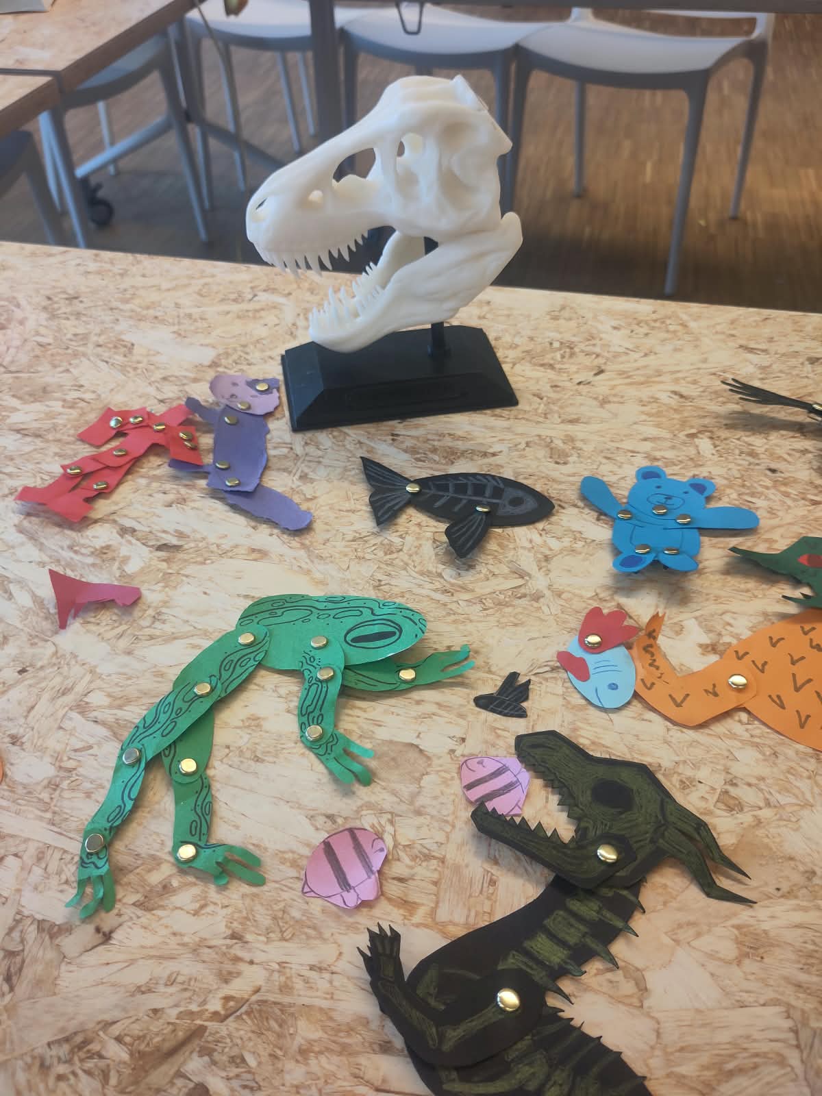 Verschillende fantasiedieren, gemaakt met splitpennen, liggen op tafel naast een 3D print van een dino skelet.