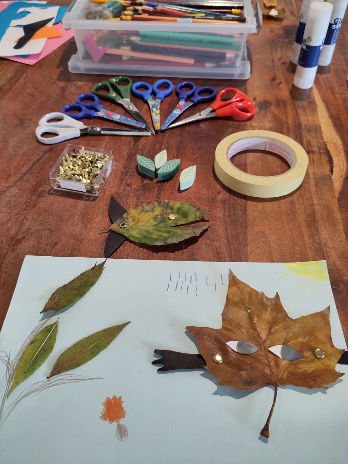 Workshopmateriaal ligt op tafel: potloden, scharen, tape, papier en herfstbladeren.