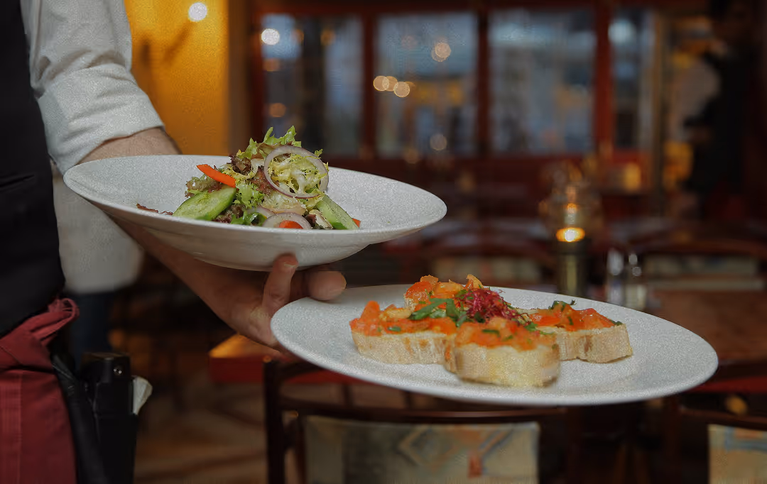 Waiter holding two plates, one with a fresh vegetable salad and the other with bruschetta topped with chopped tomatoes and herbs.