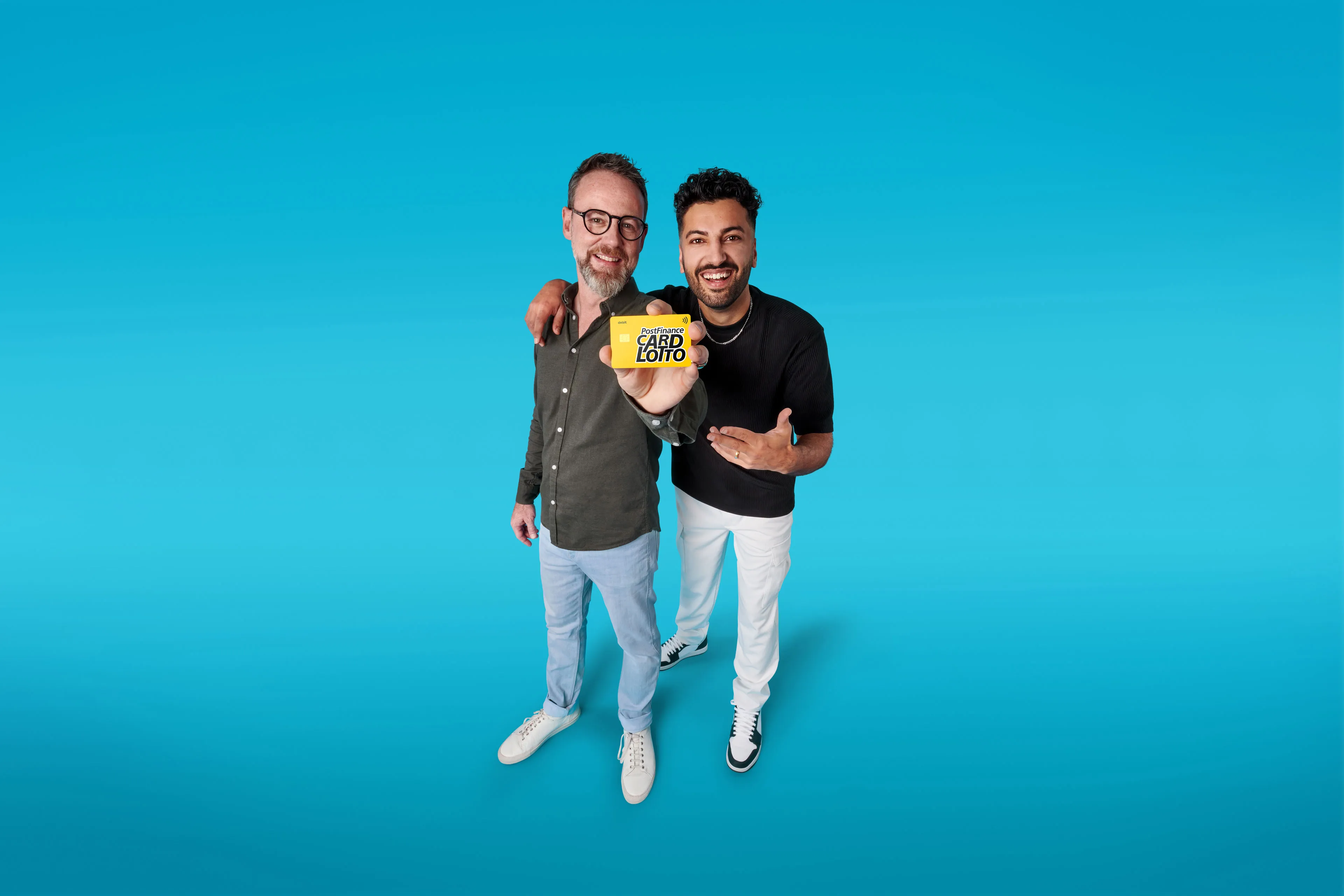 Two smiling men on blue background holding a yellow card with text 'PostFinance CARD LOTTO'.