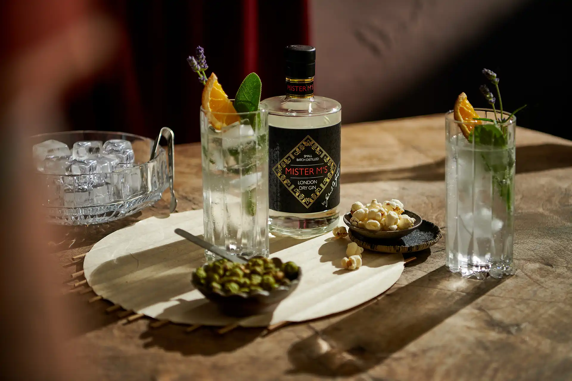 Bottle of Mister M's London Dry Gin with two gin and tonic glasses garnished with orange and lavender.