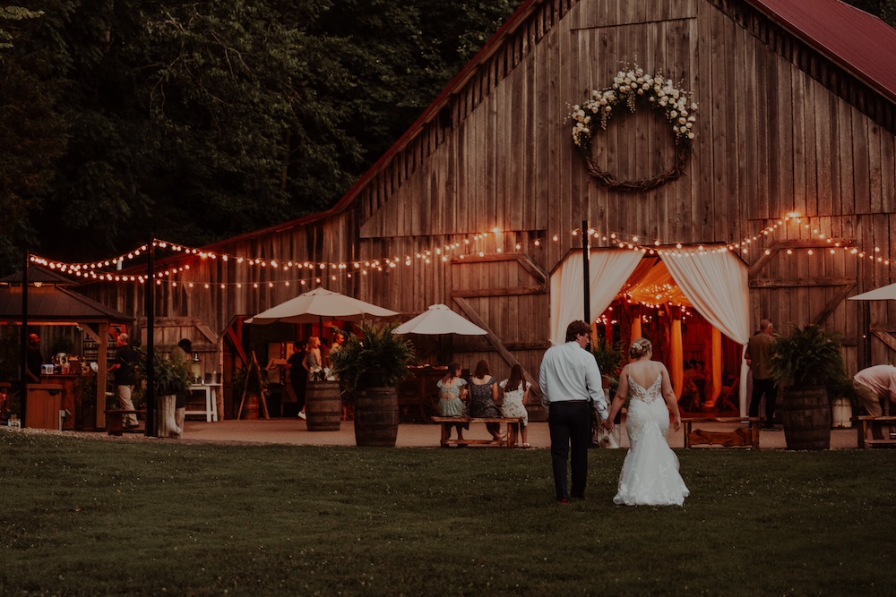 Bride and groom approach the barn reception on a beautiful evening with romantic string lights surrounding the patio at The Barn at Cedar Grove in Kentucky.