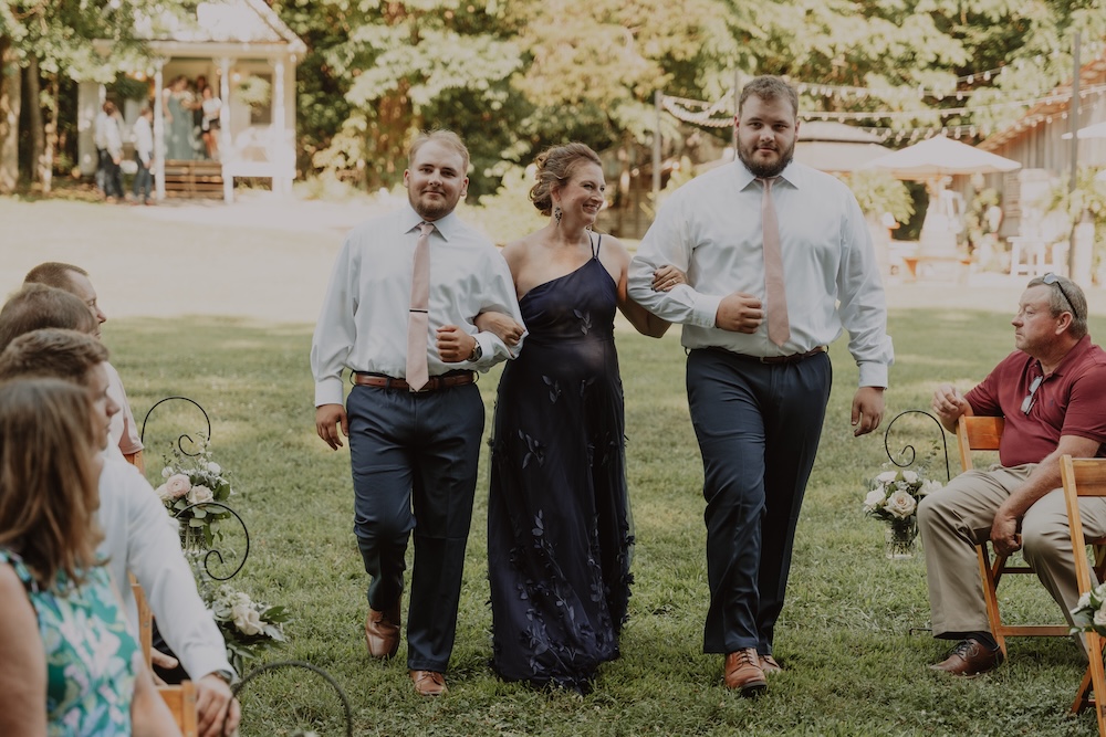 Two young men escort a mother down the wedding aisle.